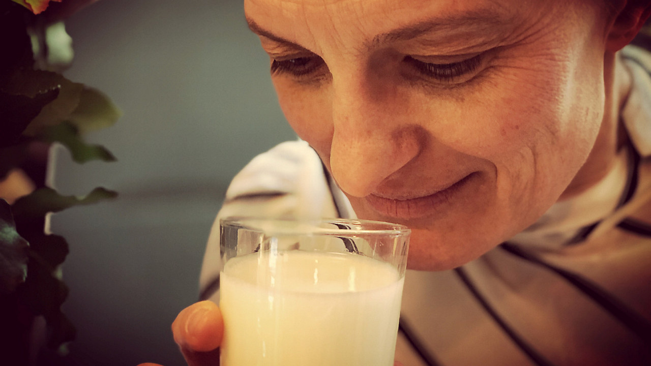 Nærbilde av person som lukter på et glass med melk for å sjekke om den er god eller ikke