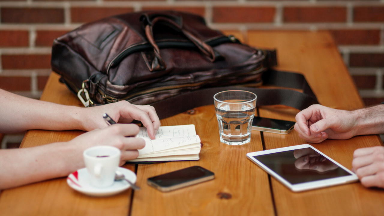 Cafebord med to kaffekopper, en veske, en Ipad og en mobiltelefon