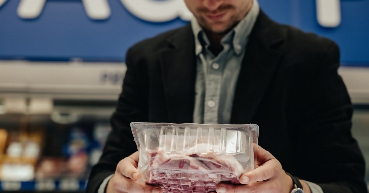 Nærbilde av kunde som leser etikett på en pakke med kjøtt.