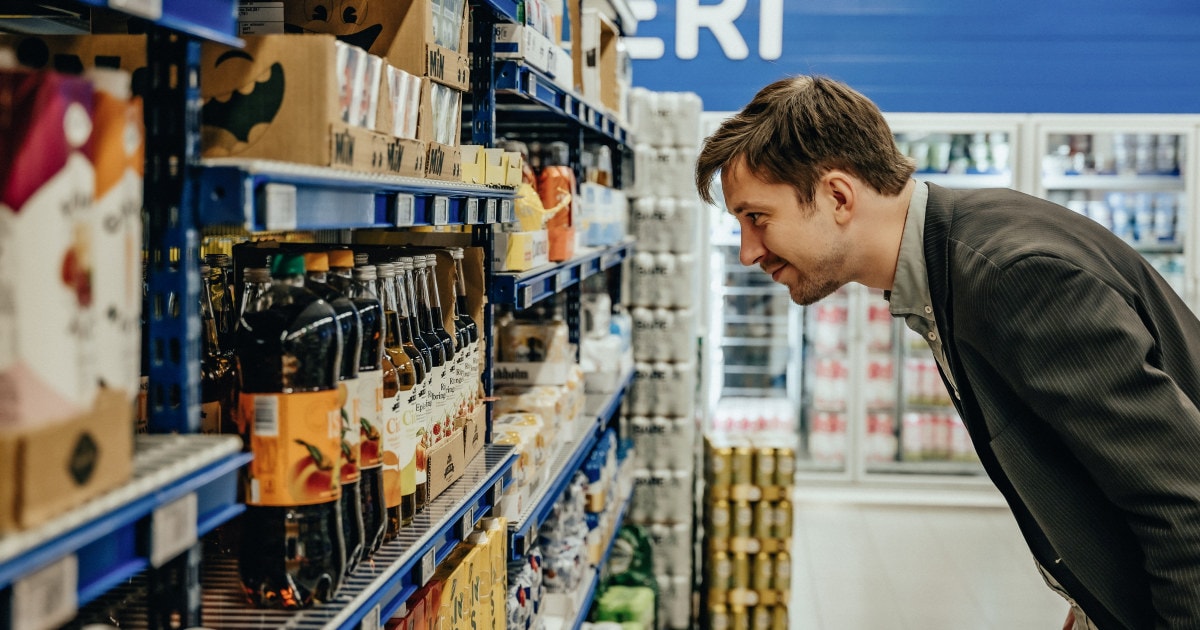 Kunde som studerer hylle med saft i dagligvareforretning.