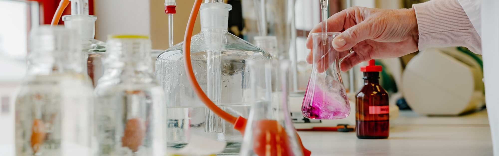 Nærbilde reagensrør med ulikt innhold i fargene rosa og gult.