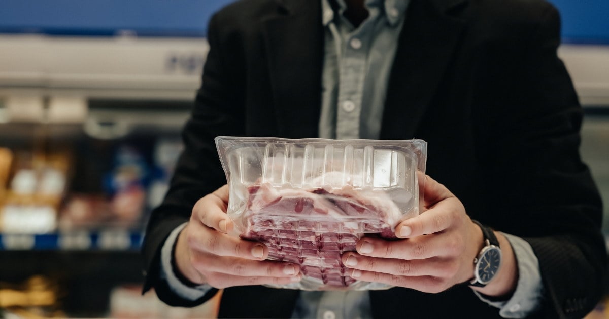 Nærbilde av kunde som leser etikett på en pakke med kjøtt.